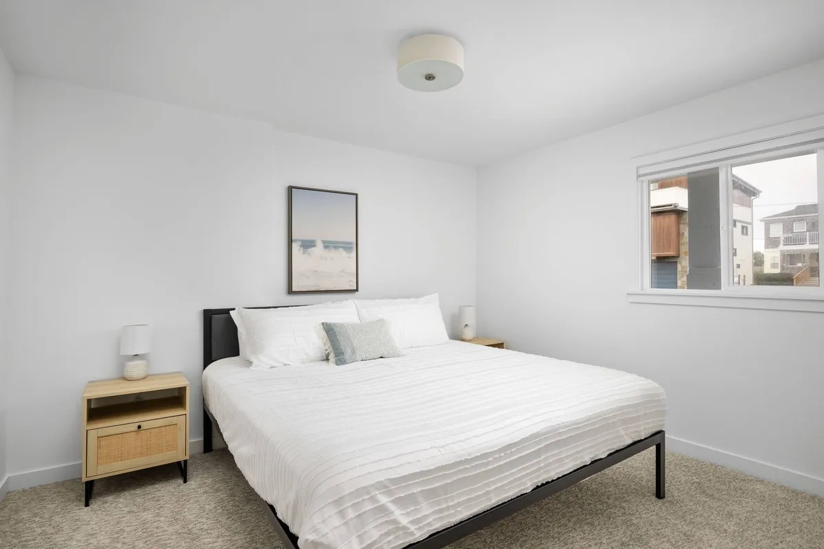 A serene bedroom scene featuring a neatly made bed with plush bedding, flanked by bedside tables and softly illuminated by natural light streaming through a window. Decorative wall art adds a touch of modern style, and the overall mood is tranquil and inviting.