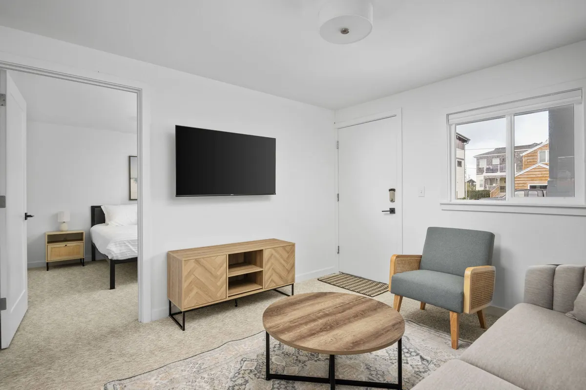 A comfortable living area featuring a sofa, coffee table, TV, and a doorway that leads into a bedroom. The space is bright and inviting, perfect for relaxing after a day at the beach. The layout suggests easy movement and a cozy atmosphere ideal for both guests and their pets.